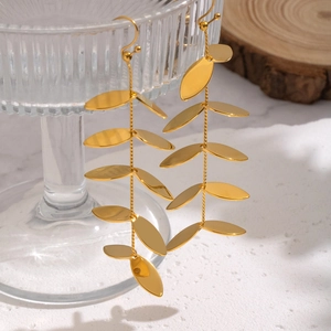 Elegant gold leaf tassel earrings in stainless steel on a white textured surface