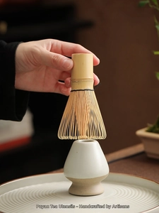 Close-up of a handmade bamboo matcha whisk and a white ceramic whisk holder set