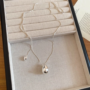 Detail showing a silver teardrop pendant necklace in a velvet jewelry box on a wood table