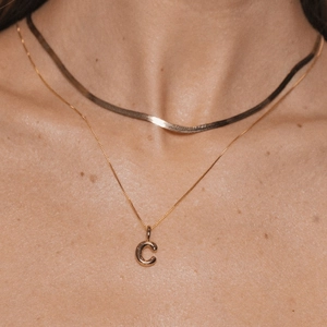 Close-up of gold-plated letter C pendant on a box chain with a flat snake chain necklace