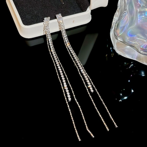 Macro detail of long silver fringe earrings with shimmering zircon pavé on black glass
