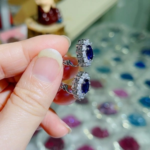Close-up of royal blue oval gemstone earrings with sparkling white zircon halo setting