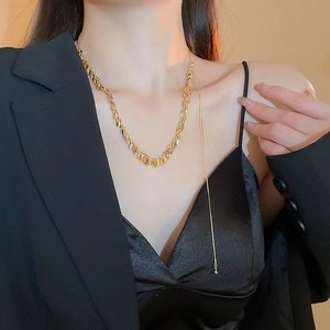 Dettaglio della collana dorata con maglie a piuma e pendente a nappa indossata dalla modella