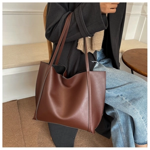 Brown leather tote bag worn over the shoulder in a minimalist indoor cafe setting