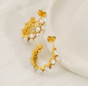Detail of gold C-shape hoop earrings with white pearls and sparkling zirconia stones