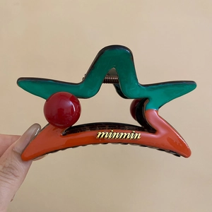 Détail d'une pince à cheveux en forme d'étoile avec un design contrasté vert et orange