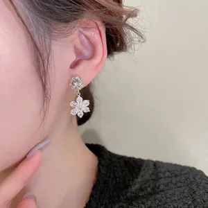 Elegant gold flower drop earrings with sparkling zircon crystals worn by a female model