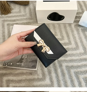 Close-up of small black and white folding wallet with golden bow and contrast stitching