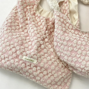 Detail of pink mesh tote bag featuring white daisy embroidery and subtle logo tag