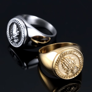 Detail view of gold and silver signet rings with prayer hands relief on black reflective surface