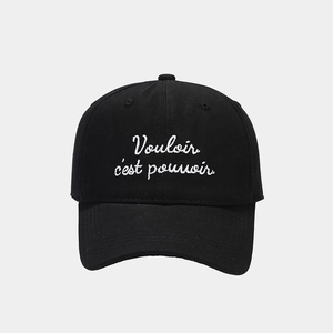 Detail of white Vouloir c'est pouvoir embroidery on a black cotton baseball cap