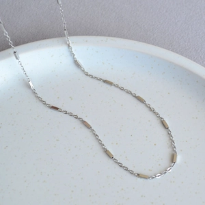 Minimalist silver geometric necklace with rectangular cubes on a white ceramic tray