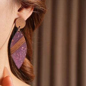 Détail de boucles d'oreilles pendantes en bois et résine violette avec dorures