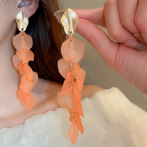 Detail view of gold leaf stud with frosted orange acrylic petal tassels worn by a model