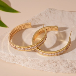 Detail of gold-tone geometric hoop earrings with cubic zirconia on a stone surface