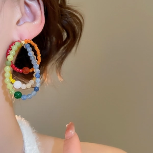 Detail of colorful multi-beaded triple hoop earrings worn on ear with soft fur collar