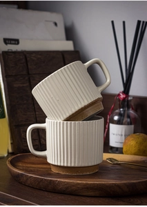 Close-up of two off-white ceramic mugs with vertical stripes and brown base on a wooden tray