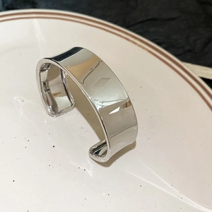 Vue détaillée d'un bracelet manchette large ouvert en argent poli sur une assiette