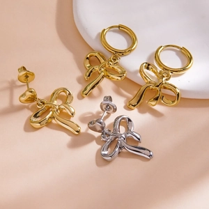 Elegant gold and silver bow drop earrings on a white tray, minimalist style