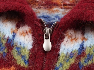 Macro shot of silver metal zipper on burgundy jacquard knit cardigan with plush texture