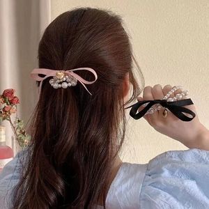 Detail of cream pearl hair tie with satin bow and gold heart pendant on model