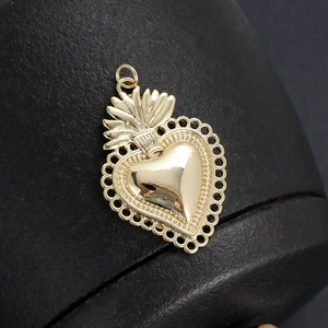 Close-up of 18K gold plated heart flame pendant with cubic zirconia inlay on black texture