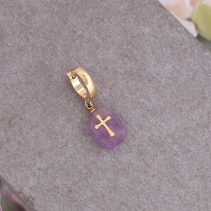 Détail d'un pendentif en pierre naturelle violette avec croix dorée sur pierre grise