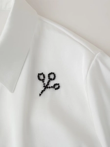Detailed view of a white collared blouse featuring a unique black beaded scissor brooch