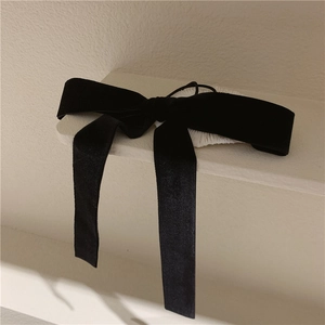 Close-up of elegant black velvet bow hair tie with long ribbons on a textured stand