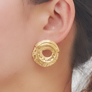 Close-up of oversized gold hoop earring with brushed and hammered metal textures