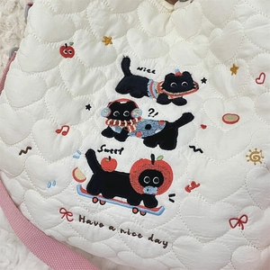 Détail du sac matelassé blanc à motif cœur avec broderie de chat noir et bandoulière