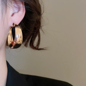 Close-up of a model wearing large polished gold chunky hoop earrings with mirror finish