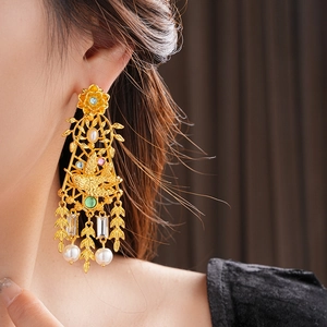 Detalle de pendientes vintage dorados con pájaros, flores y perlas en una modelo