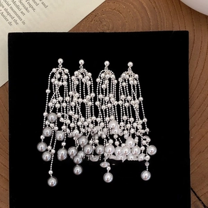 Detailed view of elegant silver tassel earrings with hanging pearls on a black velvet display