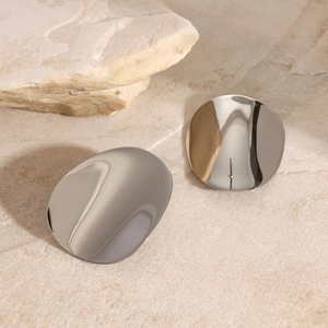Macro shot of silver polished geometric concave earrings on a textured stone surface
