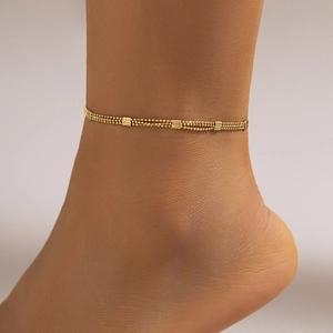 Close-up of a layered gold anklet with bead chains and rectangular textured charms