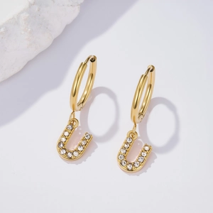 Detail of a gold U-letter earring with white cubic zirconia on a stone background