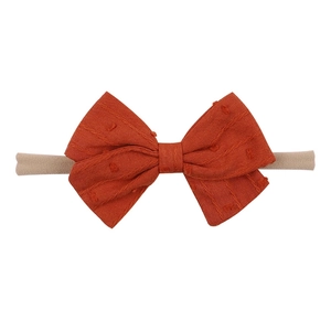 Detailed view of the orange textured fabric bow on a soft nude nylon baby headband