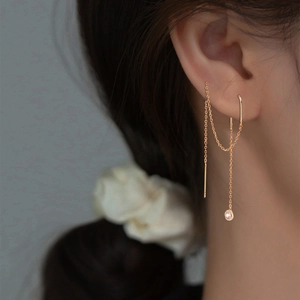 Detailed close-up of a long golden drop chain earring with a sparkling zircon stone
