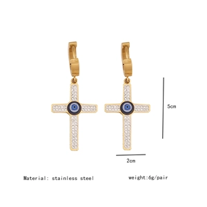 Detailed view of gold cross earrings with blue evil eye and crystal inlays, 5cm length