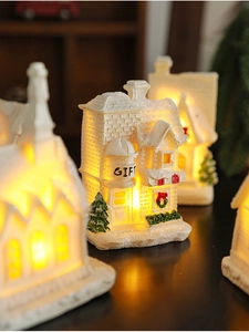 Close-up of a white resin Christmas house miniature with warm LED lighting and GIFT text