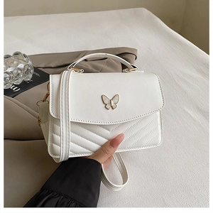 Detail of white quilted crossbody bag featuring a golden butterfly buckle and sleek V-stitching