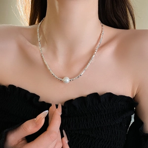 Detail of silver irregular metal beads necklace with a white pearl on woman's collarbone