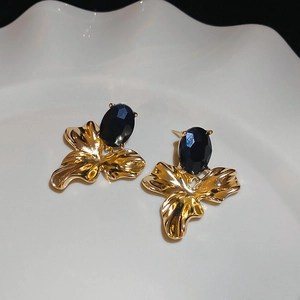 Detailed view of gold leaf earrings with large black oval crystals on white plate