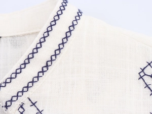 Detail of navy blue geometric cross-stitch embroidery on beige linen cotton shirt fabric