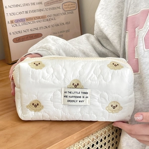 Detail of white quilted makeup bag featuring bear embroidery and orderly life quote label