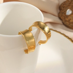 Detail of wide gold-plated chunky hoop earrings hanging on a white ceramic cup