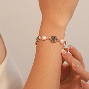 Détail d'un bracelet tournesol en or rose avec perles et cristaux foncés sur un poignet