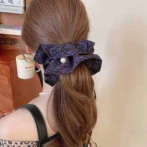 Detail of a large navy floral chiffon scrunchie with a white pearl pendant on wavy hair