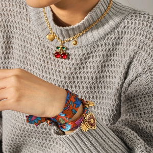 Close-up of golden necklace with red cherry pendant and vintage silk ribbon bracelet